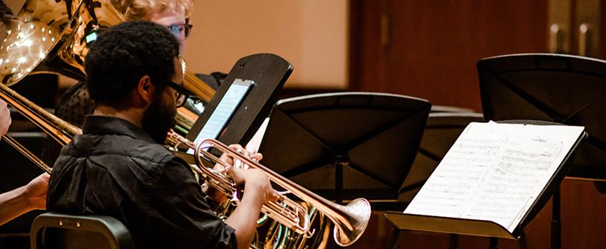 Music student playing trumpet looking at music.